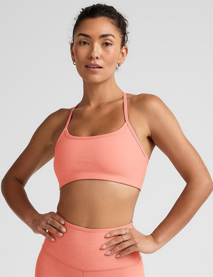 Woman wearing a coral sports bra and leggings set on a light gray background.