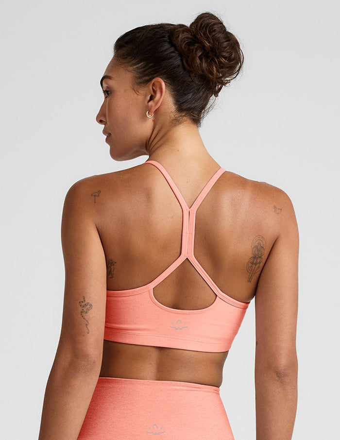 Woman wearing a coral sports bra and leggings set on a light gray background.