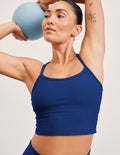 Woman in a blue cropped top and leggings holding a blue ball against a light background.