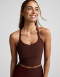 Woman wearing a brown racerback cropped tank top and brown high-waisted midi length leggings against a plain background.
