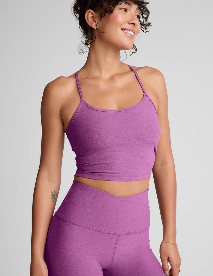 Woman wearing a purple cropped tank and leggings on a gray background.