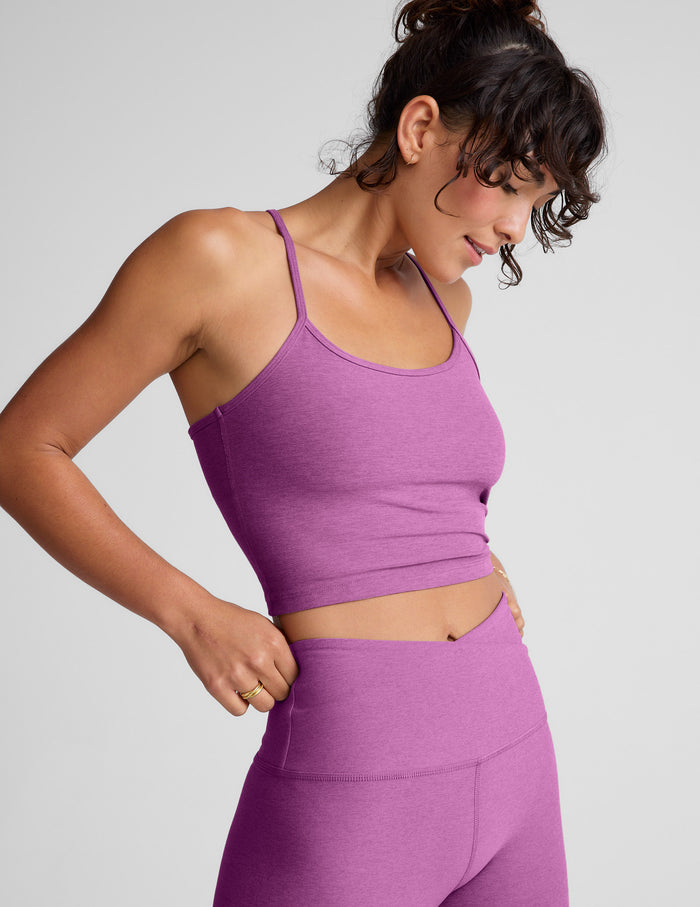 Woman wearing a purple cropped tank and leggings on a gray background.