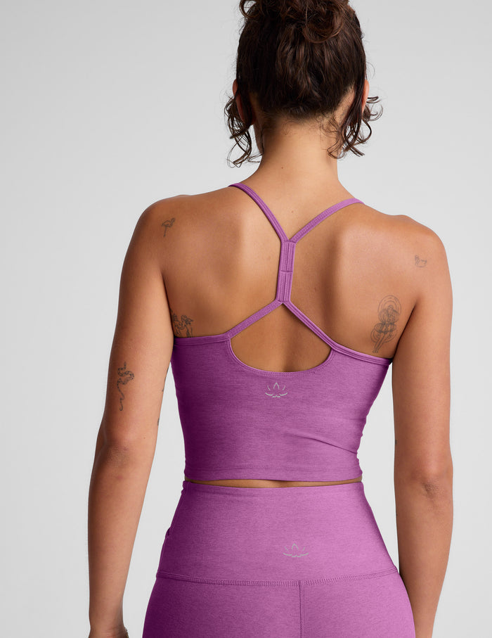 Woman wearing a purple cropped tank and leggings on a gray background.