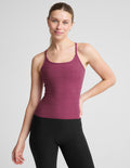 A woman modeling a heathered magenta racerback tank top paired with black leggings, photographed against a solid light gray studio background.