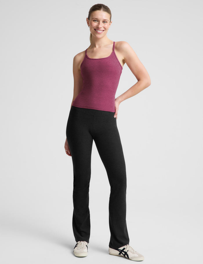 A woman modeling a heathered magenta racerback tank top paired with black leggings, photographed against a solid light gray studio background.