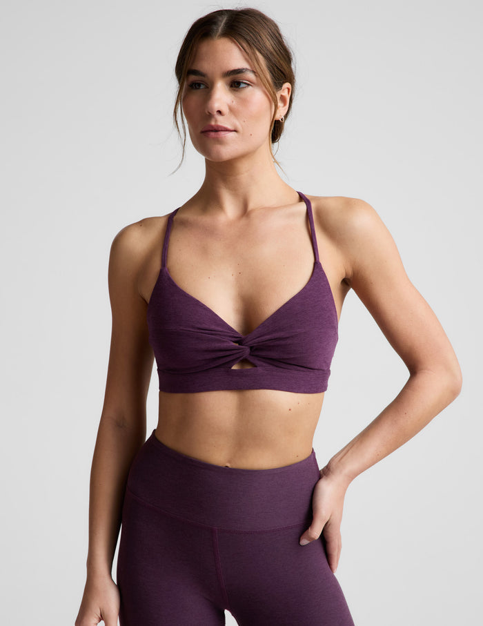 Woman wearing a purple sports bra and leggings on a light gray background.