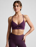 Woman wearing a purple sports bra and leggings on a light gray background.