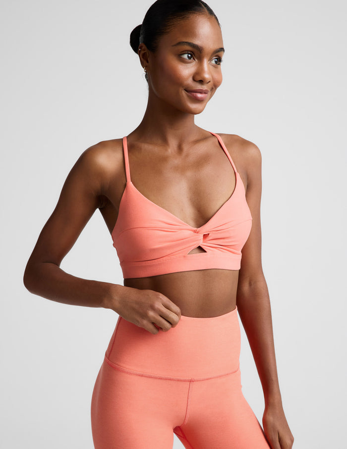 Woman wearing a coral sports bra and leggings on a light gray background.