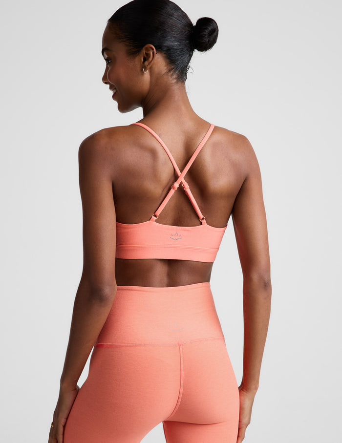Woman wearing a coral sports bra and leggings on a light gray background.