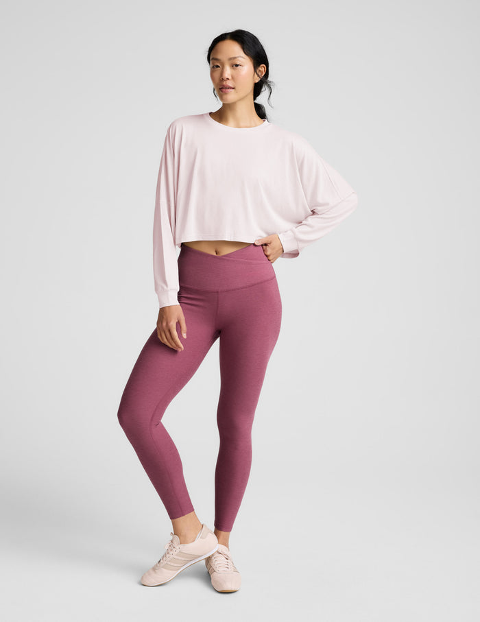 Woman wearing a pink long-sleeve top and mauve leggings indoors.