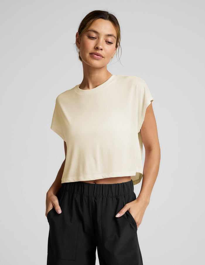 Woman wearing a cream colored cropped tee and black pants against a plain background.