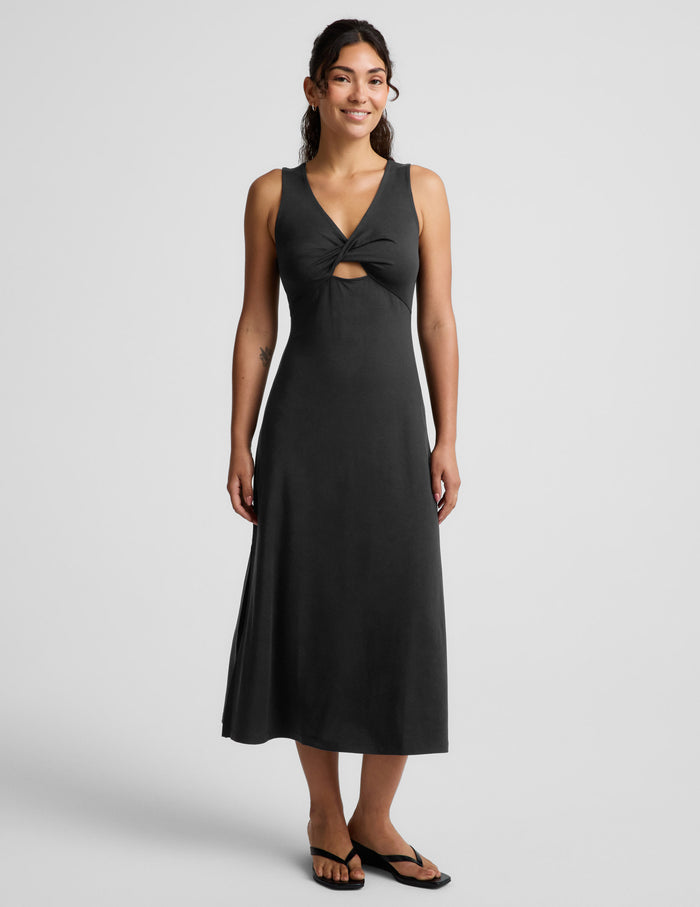 Woman wearing a black sleeveless midi dress with a cutout design on a light gray background.